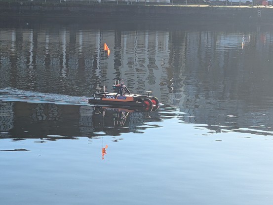 A research car/boat floating on a dock. It has a tall little orange flag on the back and wheels at the front.