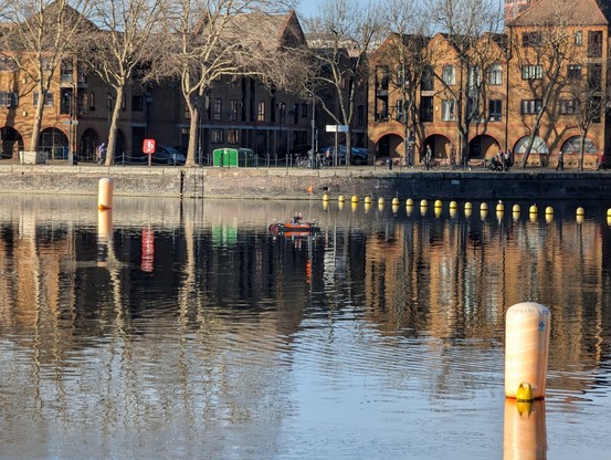 Greenland Dock, London, with a buoy in the foreground and residences reflected in the water surface. A small research vessel floats in the centre.