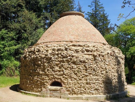 A 14m wide stone cylinder topped by a conical brick cupola sits on flat bare ground surrounded by woodland