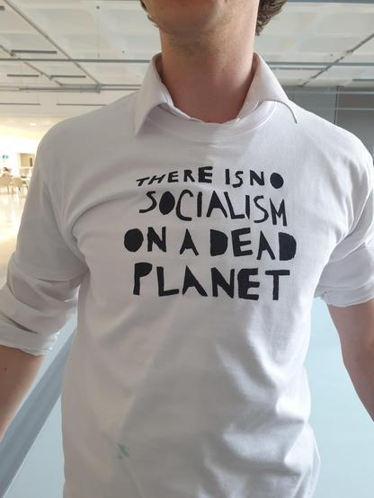 Torso shot of young adult wearing white long-sleeved T-shirt bearing slogan in black ink: 'there is no socialism on a dead planet'