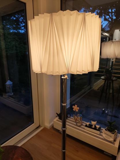 Die Leuchtende Lampe nun aufrecht stehend. Im Hintergrund sieht man 2 große Fenster und einen kleinen Heizkörper.